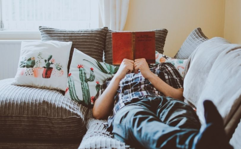 Man lying on sofa reading book
