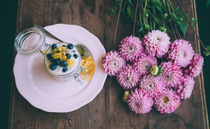 Yoghurt and blueberries on a table with flowers